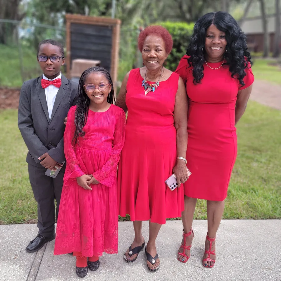 Executive Director Titania Lamb, on the right, smiles outdoors with three family members, all dressed in red and formal wear
