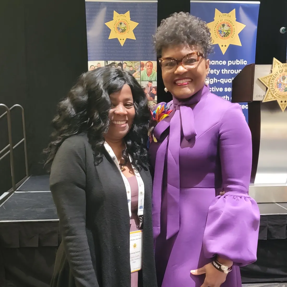 Two women smile together in front of public safety banners at a juvenile justice event