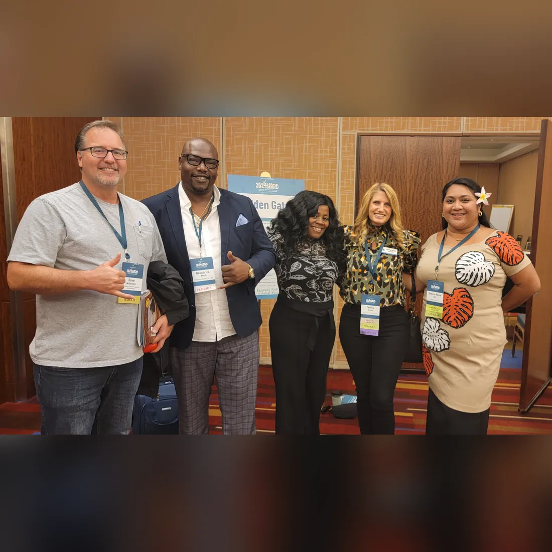 Five training attendees with name badges give a thumbs up at a conference