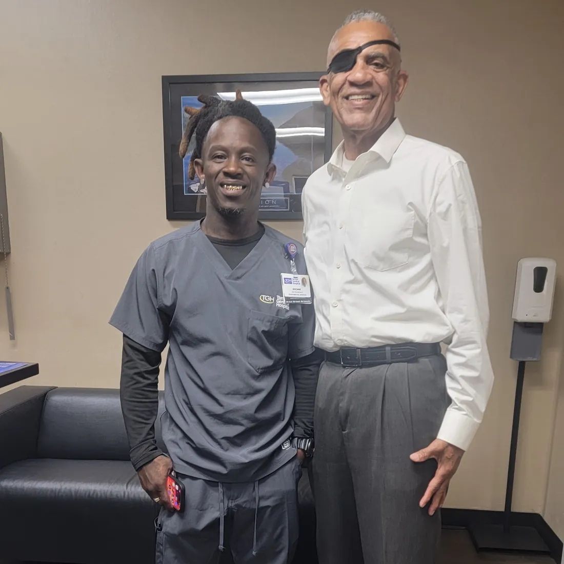 A smiling program participant in hospital work scrubs stands beside a man in a white dress shirt