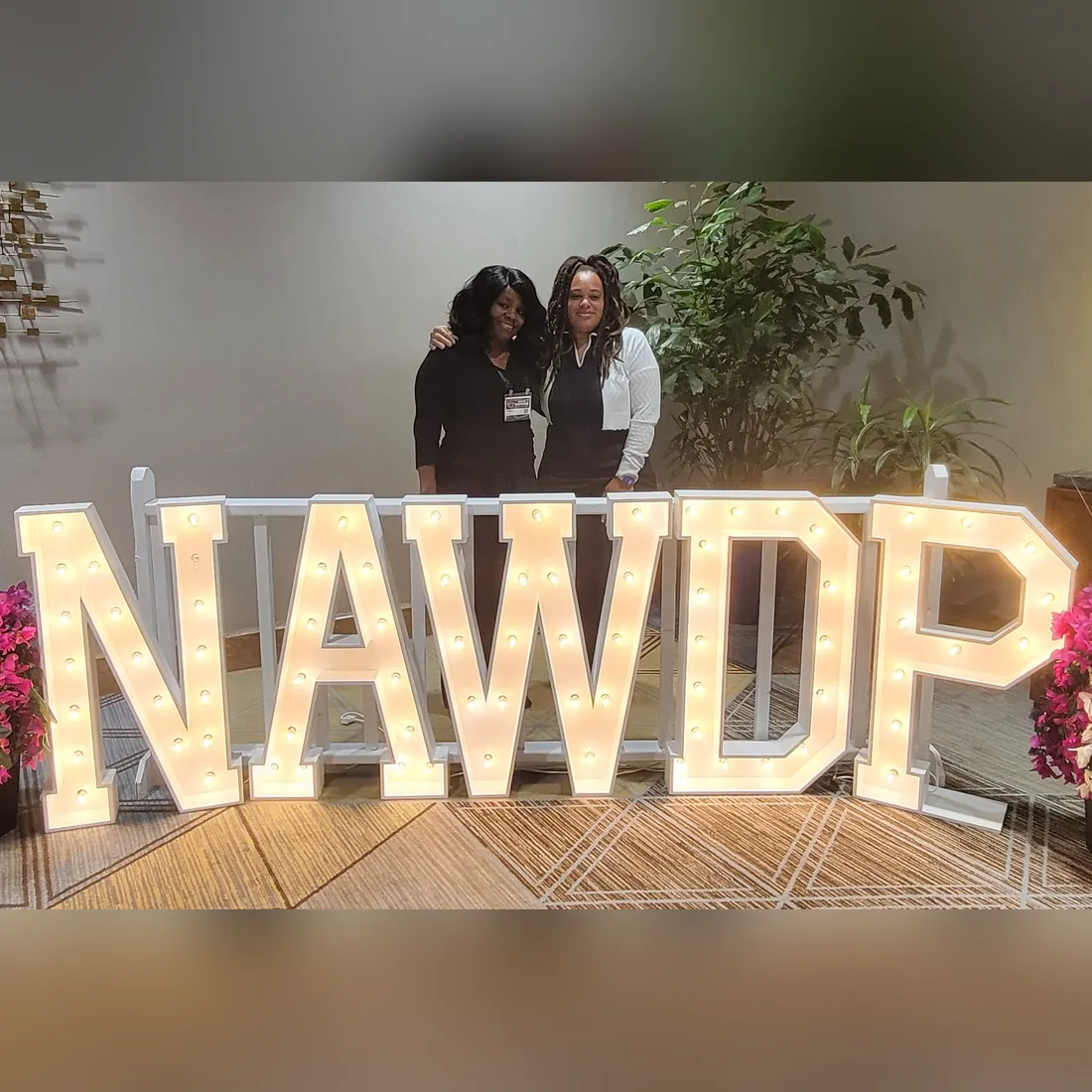 Two attendees smile behind large lighted NAWDP letters at the National Association of Workforce Development Professionals conference