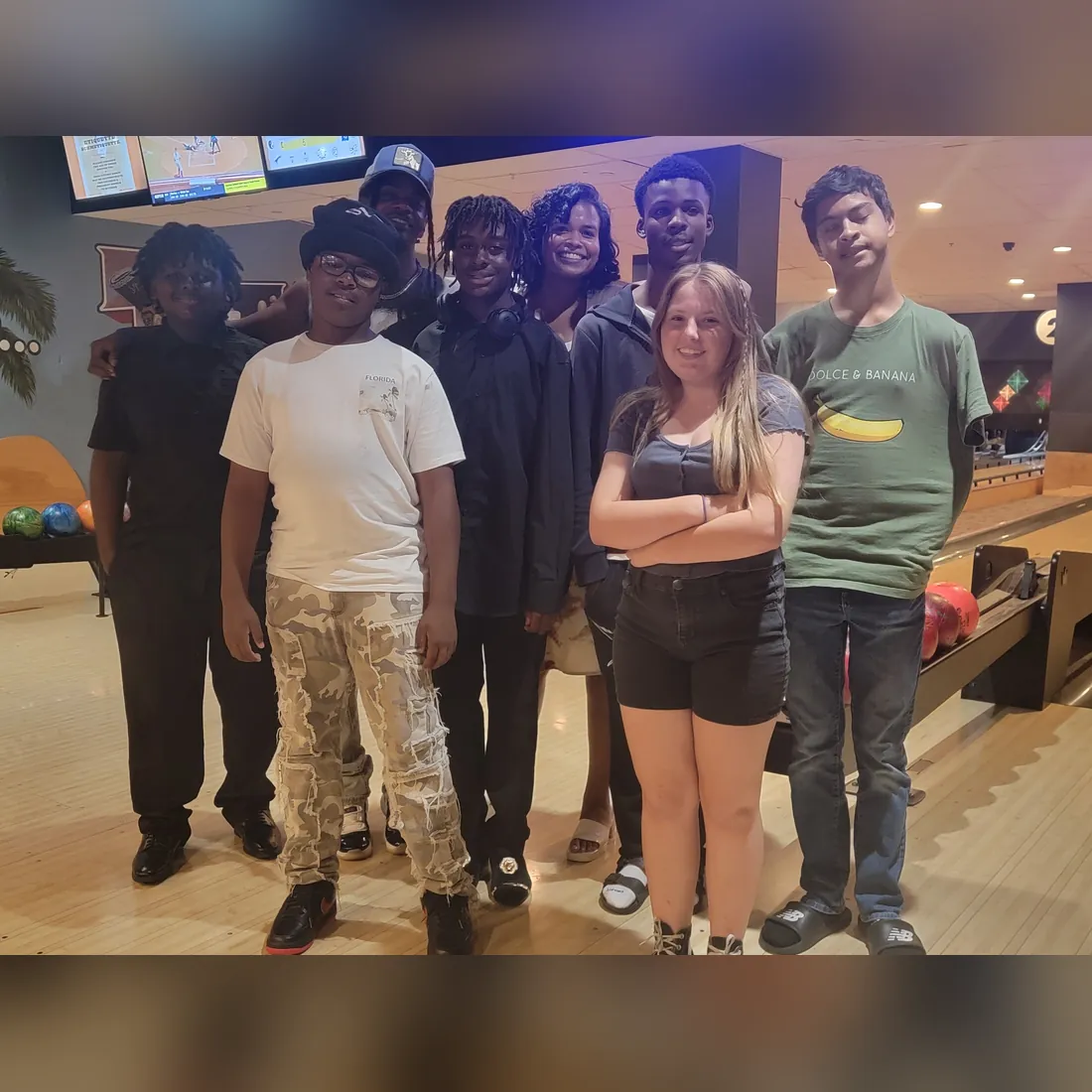 A group of TBAH youth and a youth leader smile together at a bowling alley